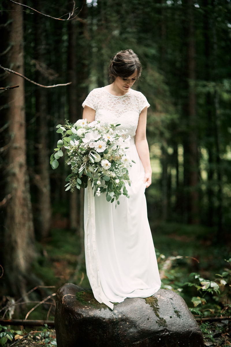 Braut mit großem Brautstrauß und weißem Spitzenbrautkleid im Wald